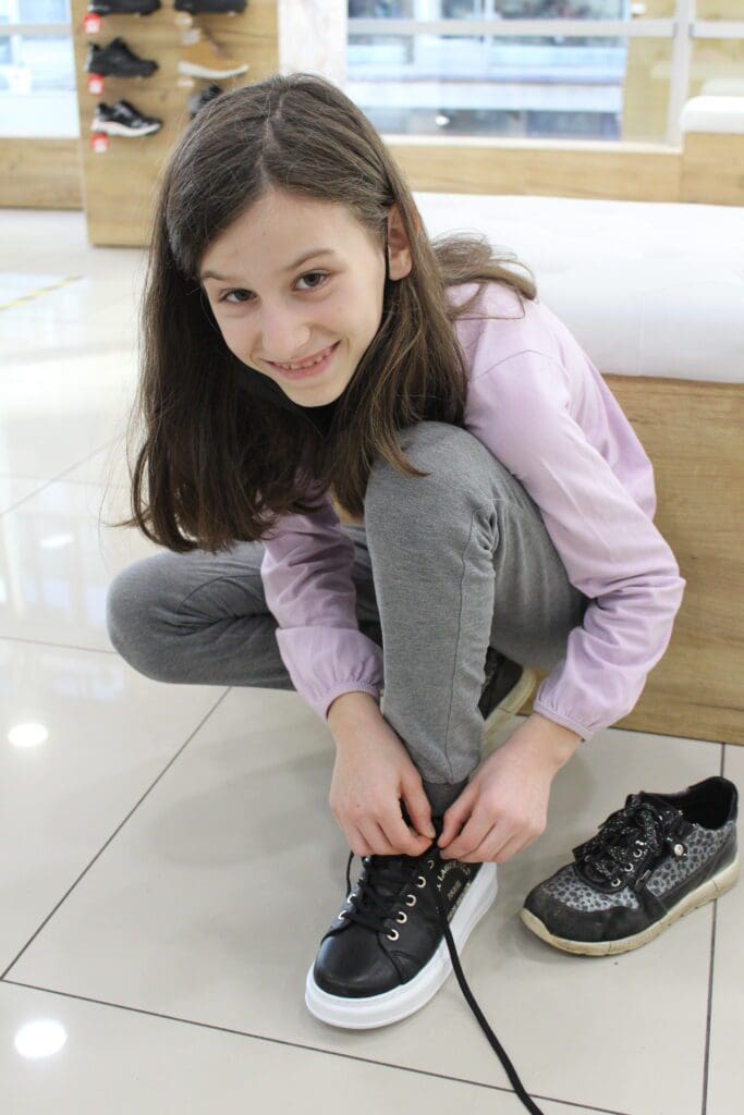 Smiling girl trying on sneakers in shoe store