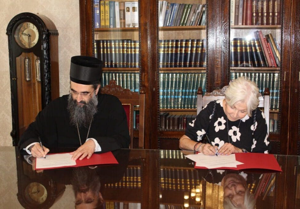 Two people signing documents in front of bookshelves